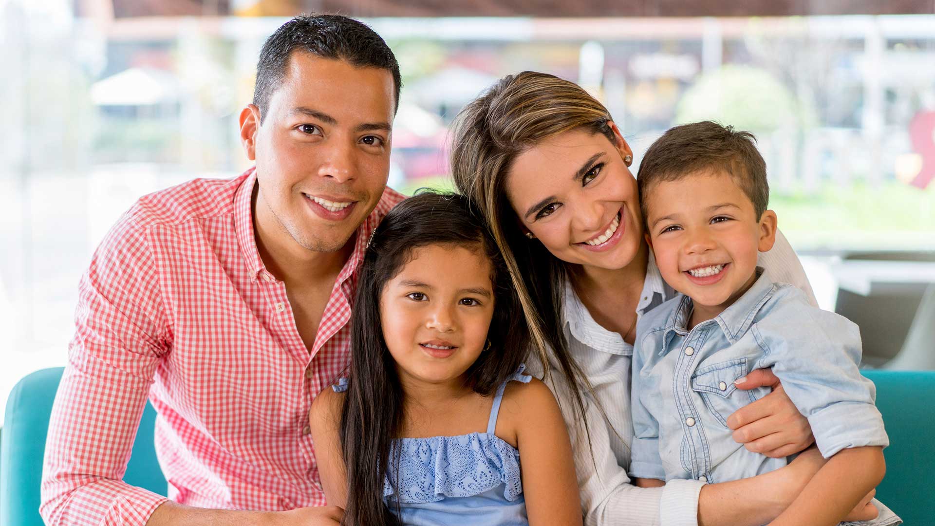 Smiling family of four, including a mother, father, daughter, and son, sitting closely together indoors, showcasing the warmth and togetherness emphasized by Miami Mental Health in supporting strong family bonds and emotional well-being