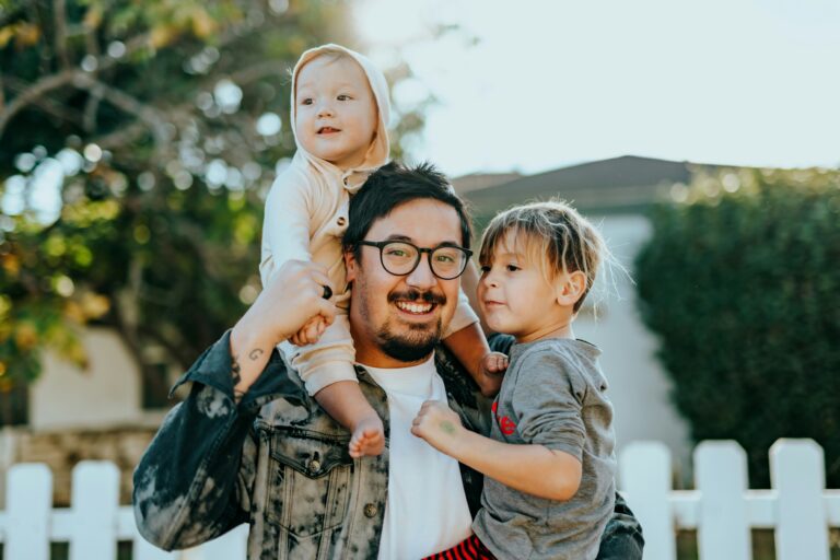 "A happy father with glasses, holding his two young children outdoors, capturing the essence of family joy and Miami Mental Health."